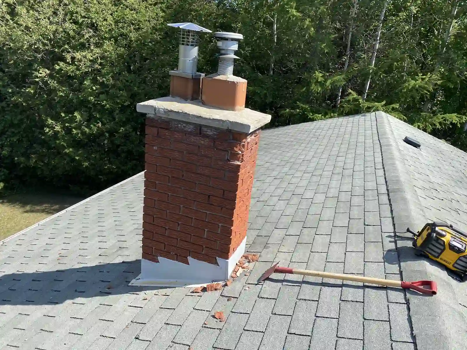 Brick chimney on a grey shingle roof with tools nearby